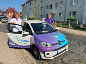 Zwei lächelnde Teammitglieder des Diako Pflegedienstes Eisenach stehen am Dienstauto mit Diako Thüringen Beklebung